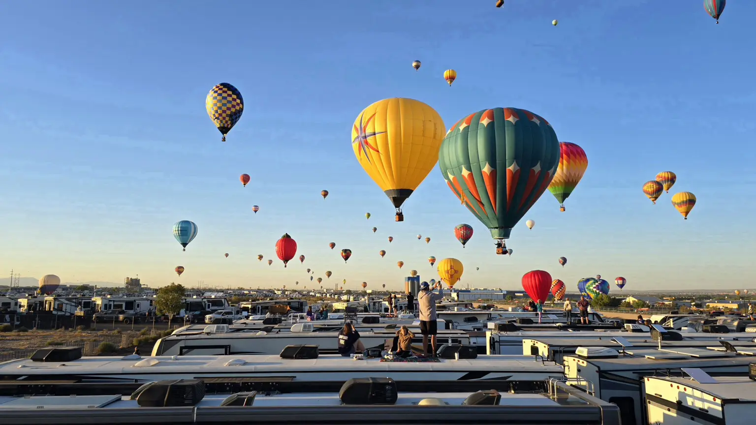 Hot-air balloons rising over a field of RVs at dawn